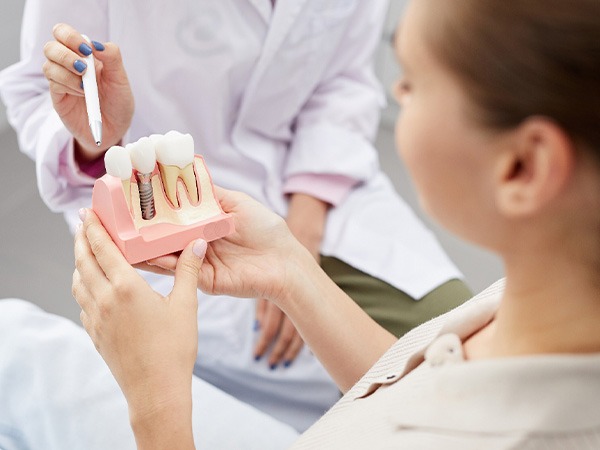 Dentist pointing to model of a single dental implant held by patient