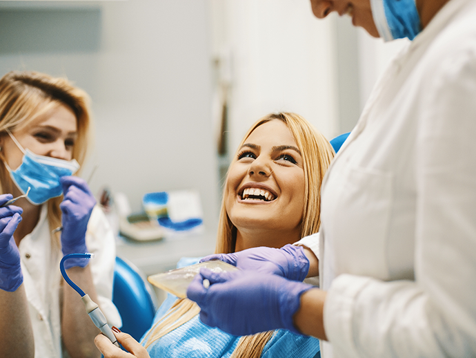 Woman in dental chair grinning up at her dentist