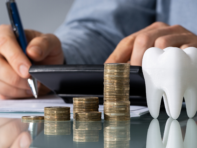 Person typing on a calculator on a desk with stacks of coins