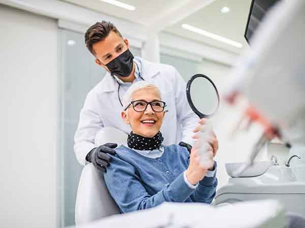 An older woman in a dentist’s office admiring her new smile