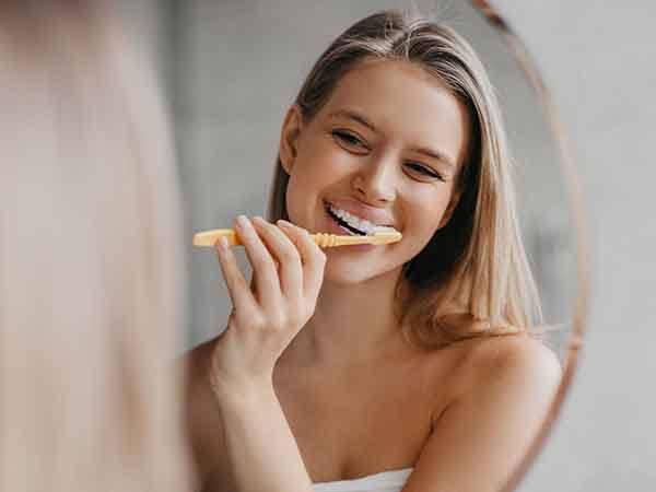 A woman brushing her teeth in front of a bathroom mirror