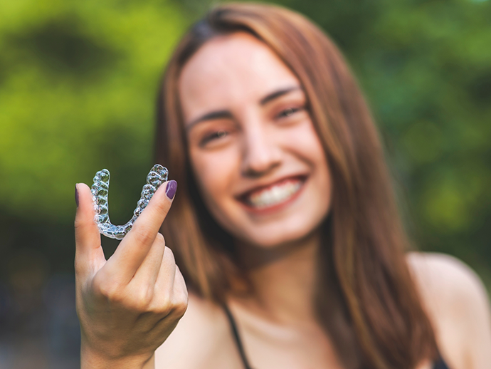 Smiling woman holding an Invisalign aligner