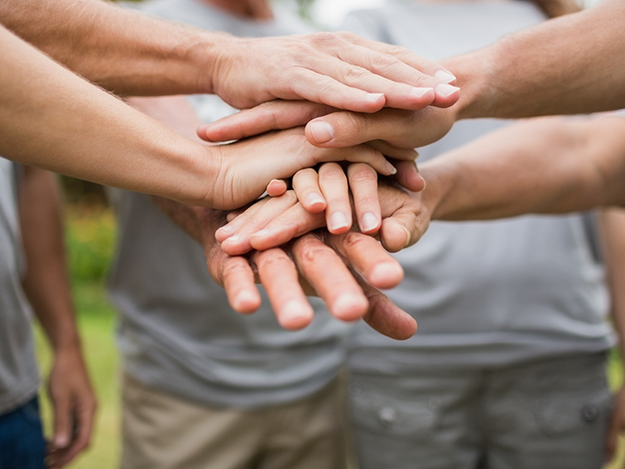 Group of people standing in a circle and placing their hands together in the middle