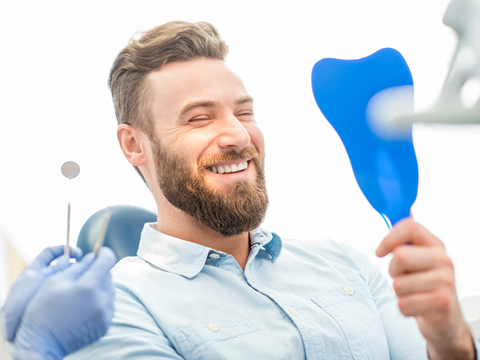 Bearded man in dental chair looking at his smile in a mirror