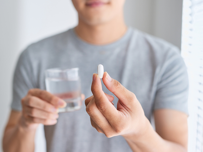 Person taking a white pill with a glass of water